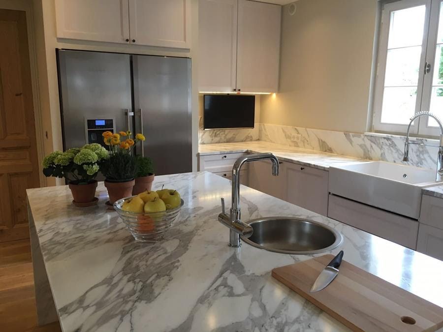 Modern kitchen with marble countertops, a sink, fruit bowl, and potted plants.